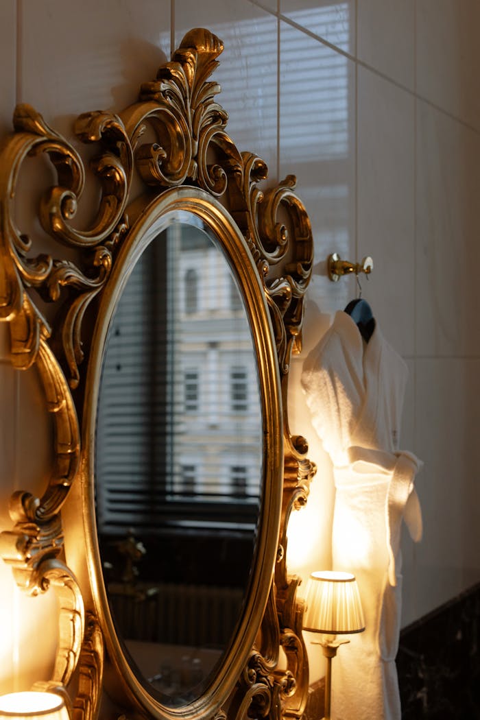 Classic Oval Mirror Hanging on Wall Beside Two Lighted Lamps and Bathrobe